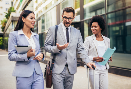 Three young business people walking and talking outdoors.